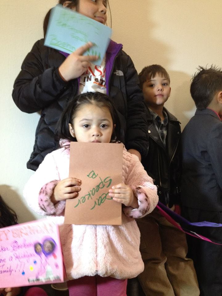 One young girl holds a handmade card upside-down that reads. "Dear Speaker B."